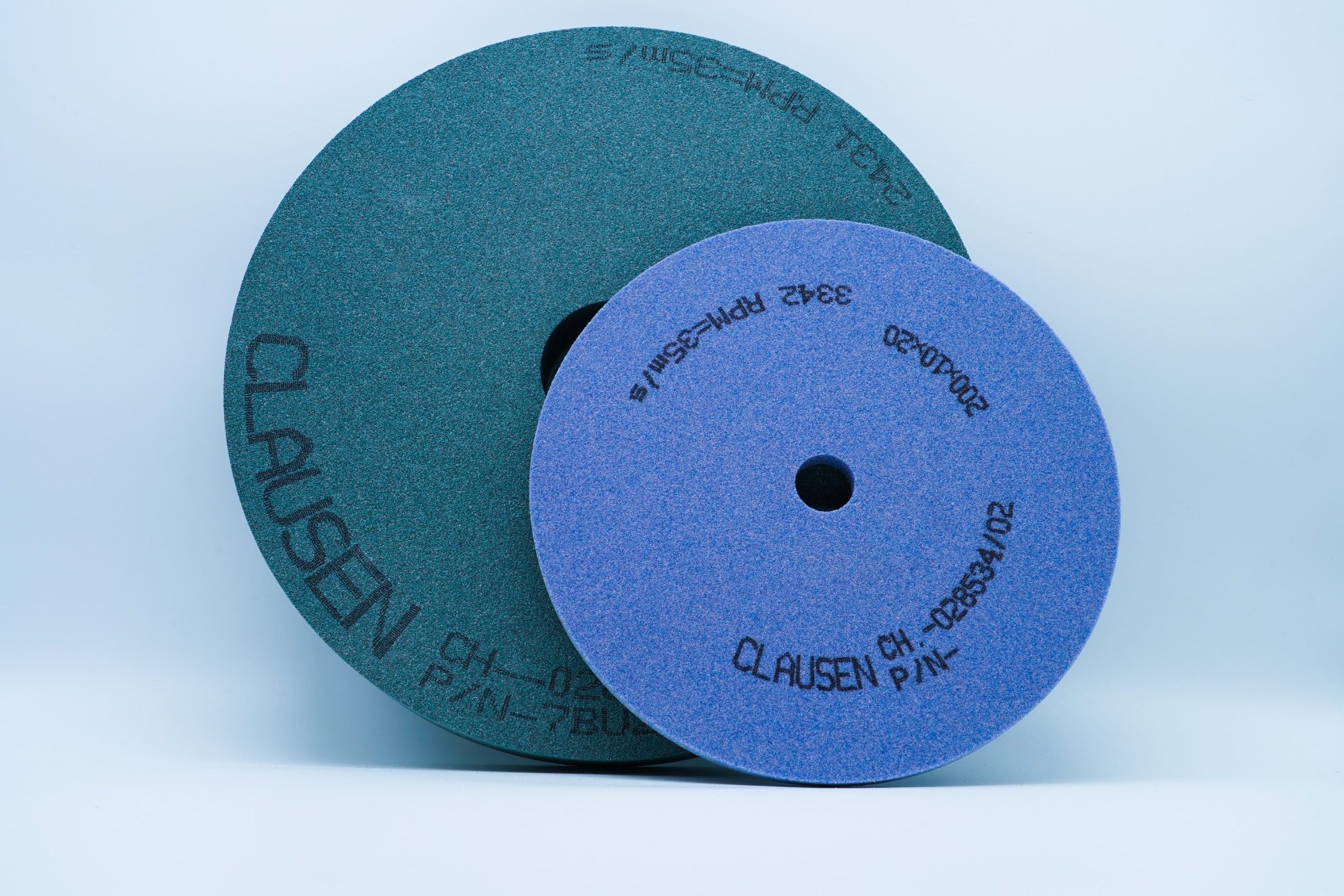 Zwei Schleifscheiben in grün und lila, übereinander gestapelt auf hellem Hintergrund.